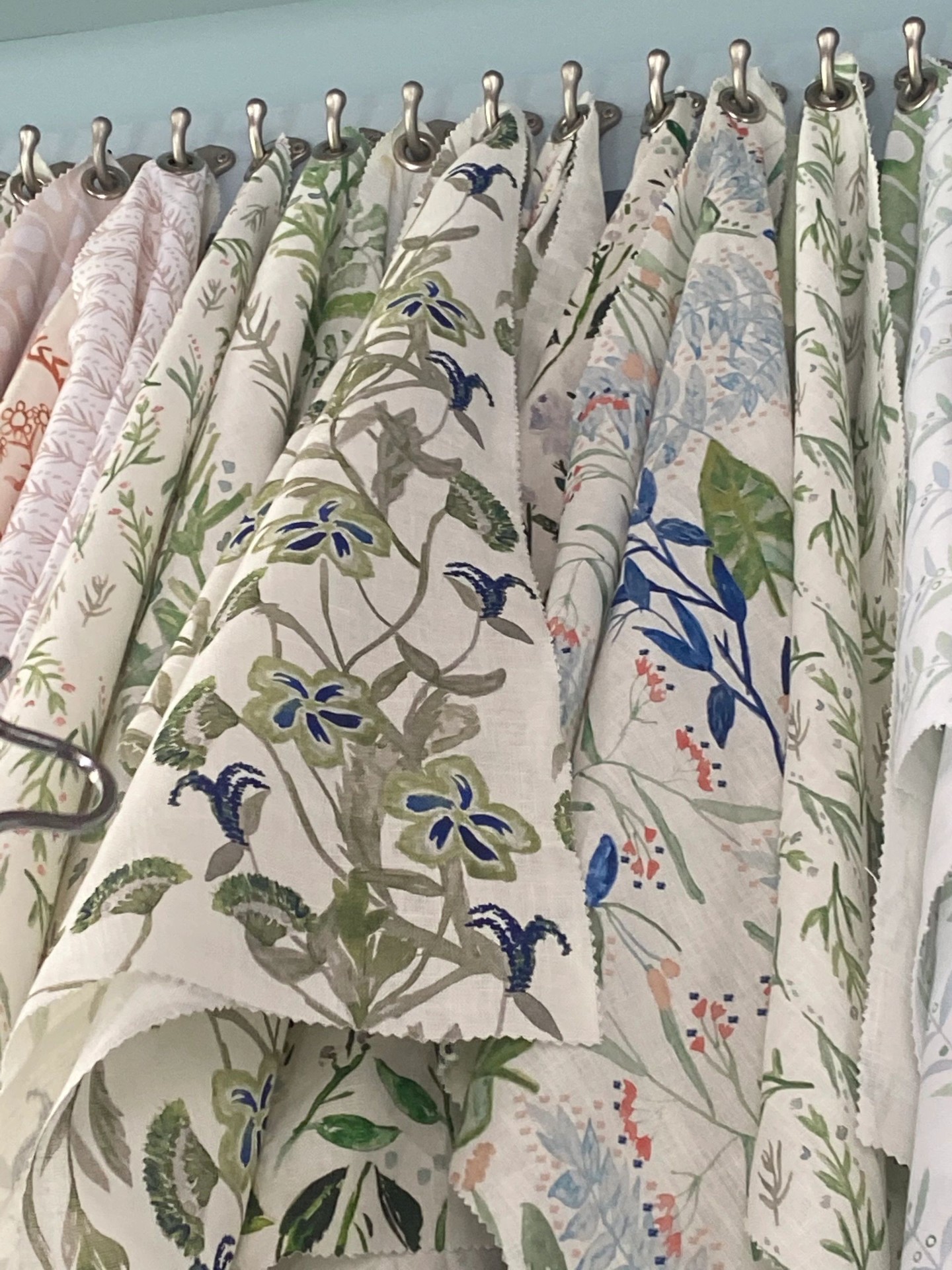 Rack of botanical and floral drapery fabric samples in greens, blues, and blush