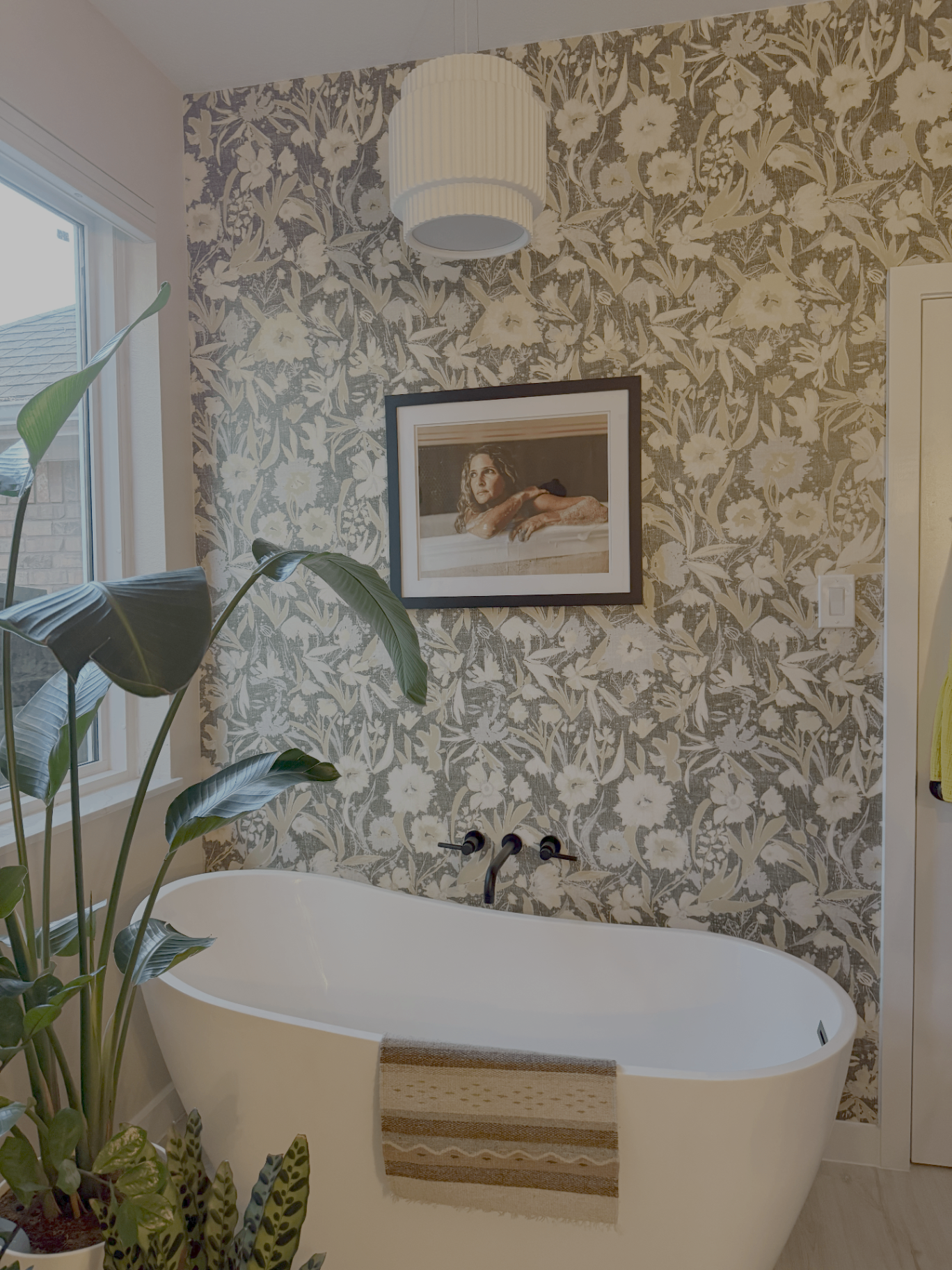 Freestanding tub against botanical wallpaper with pendant light and bird-of-paradise plant