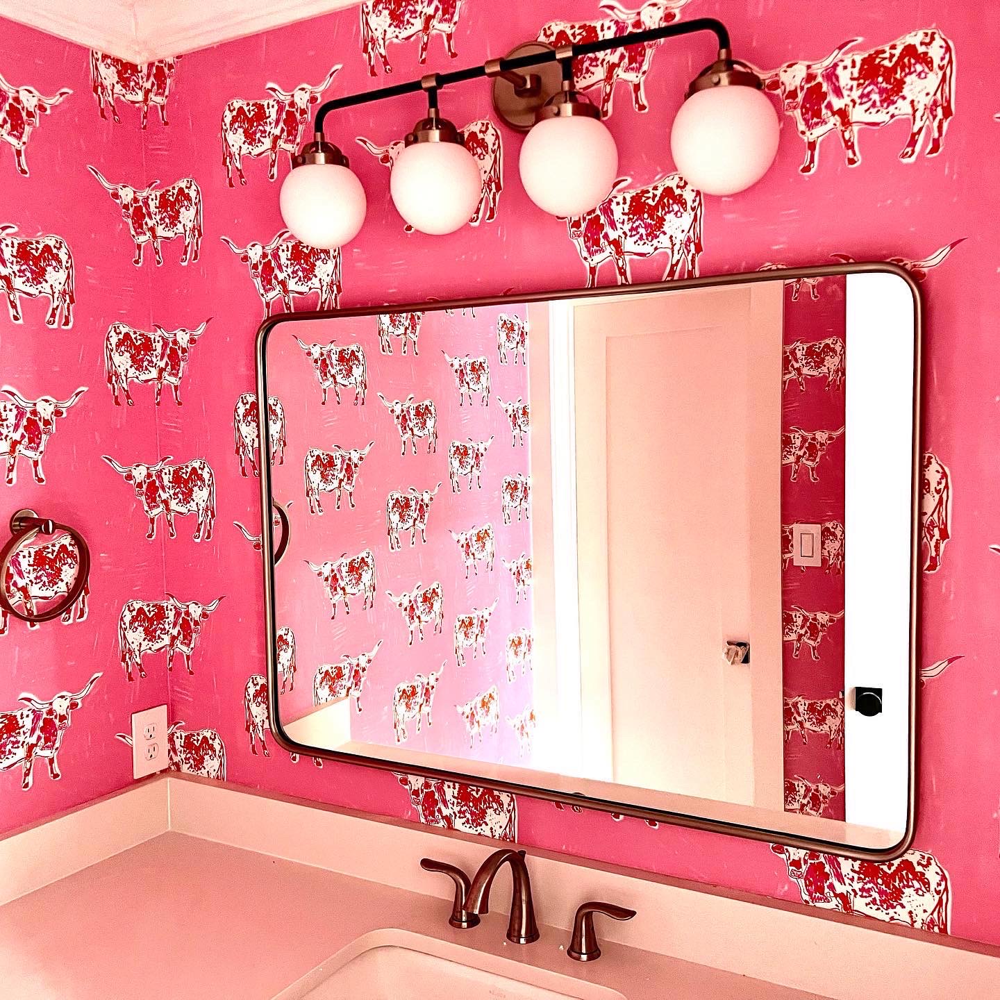 Powder room with hot pink longhorn wallpaper, brass mirror, and globe vanity lights