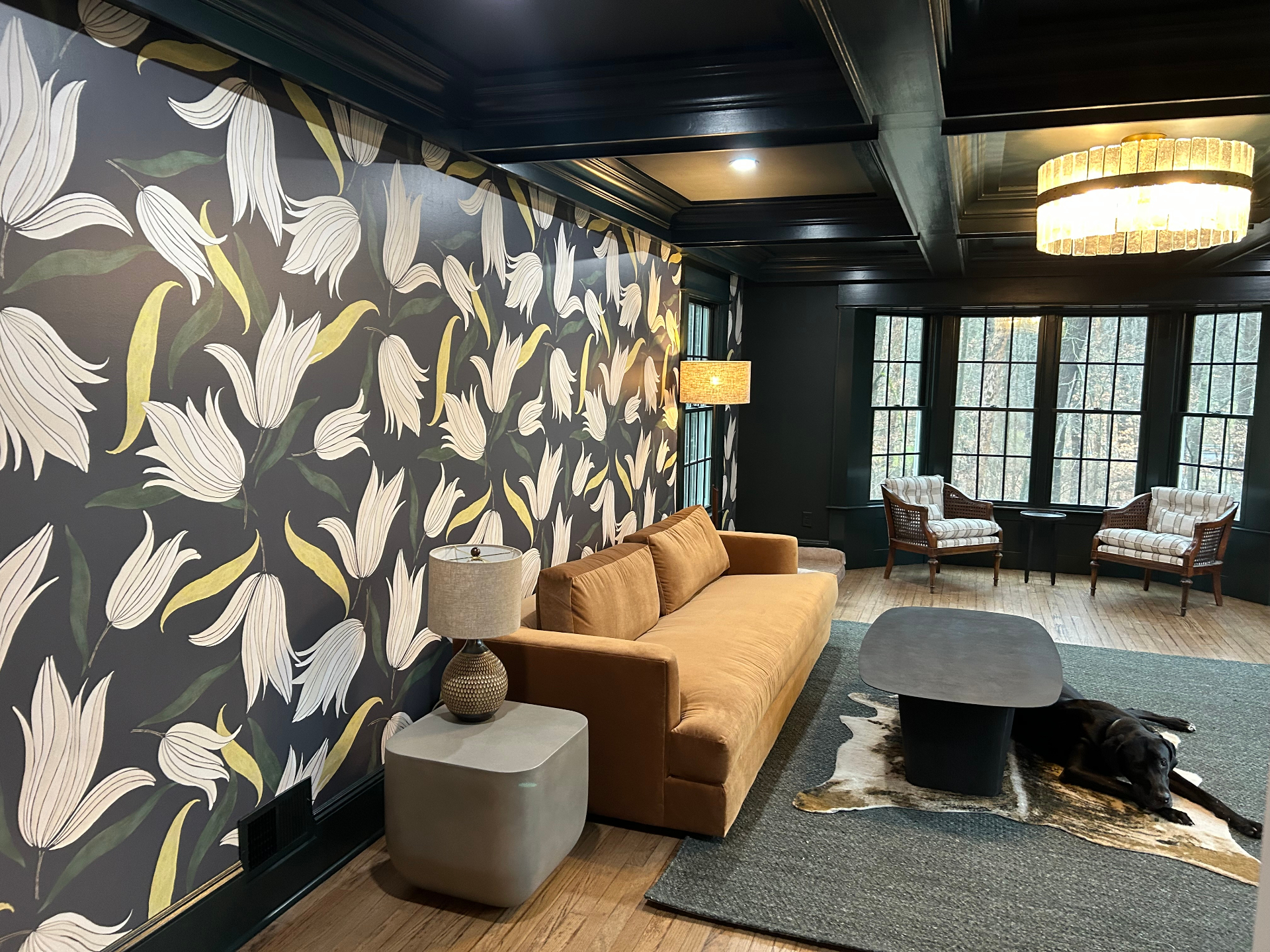 Moody lounge with oversized white tulip wallpaper, coffered navy ceiling, and rust velvet sofa