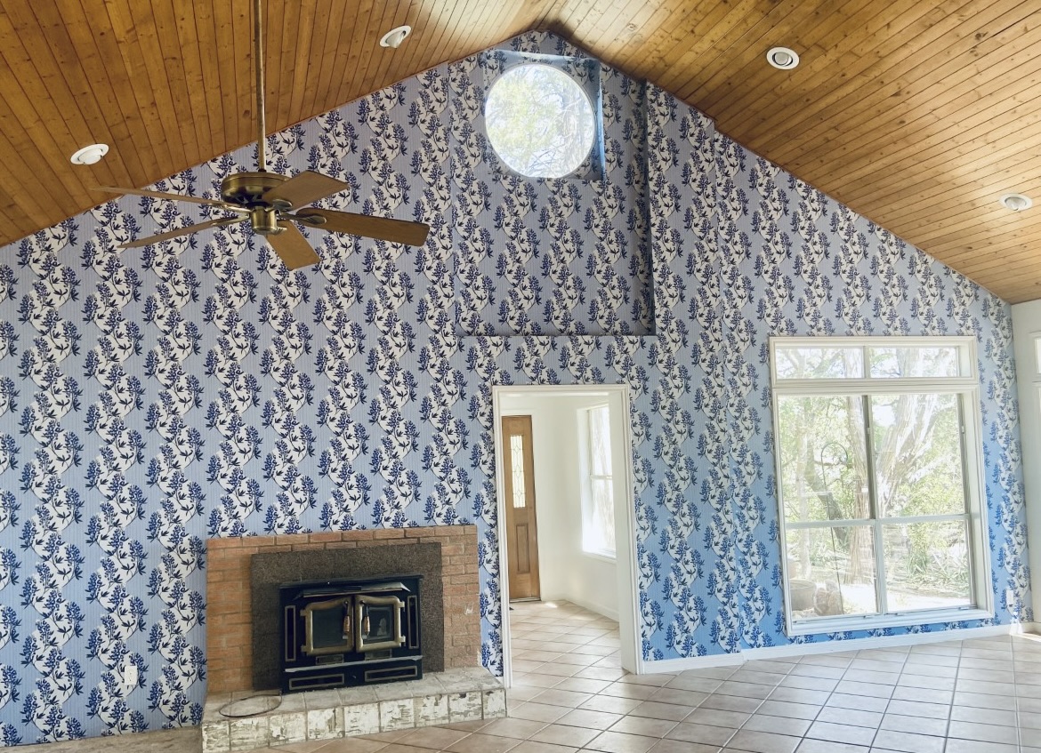 Vaulted living room with blue bluebonnet floral wallpaper, wood ceiling, and brick fireplace