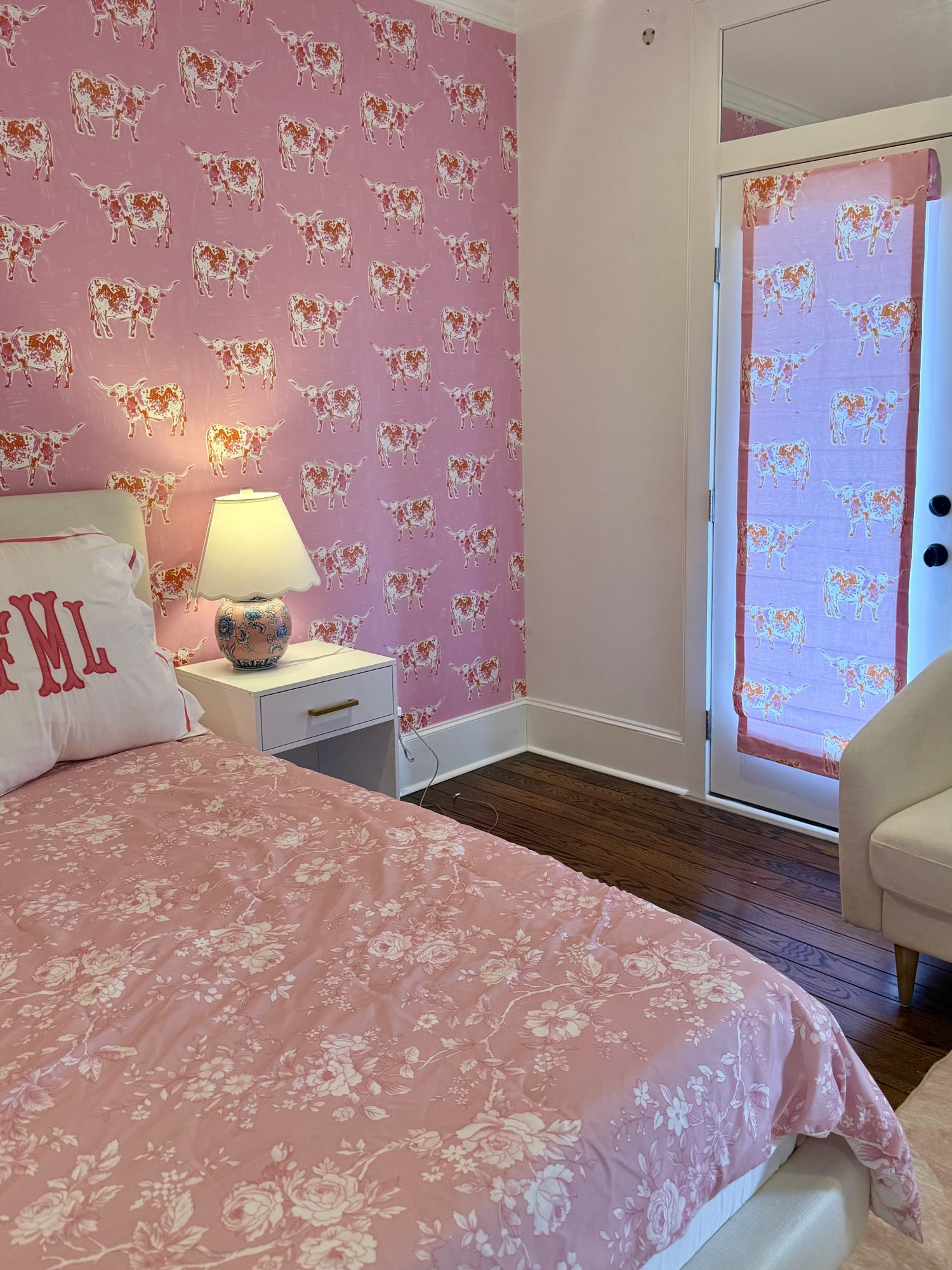 Bedroom with pink longhorn wallpaper, matching Roman shade, and floral bedding