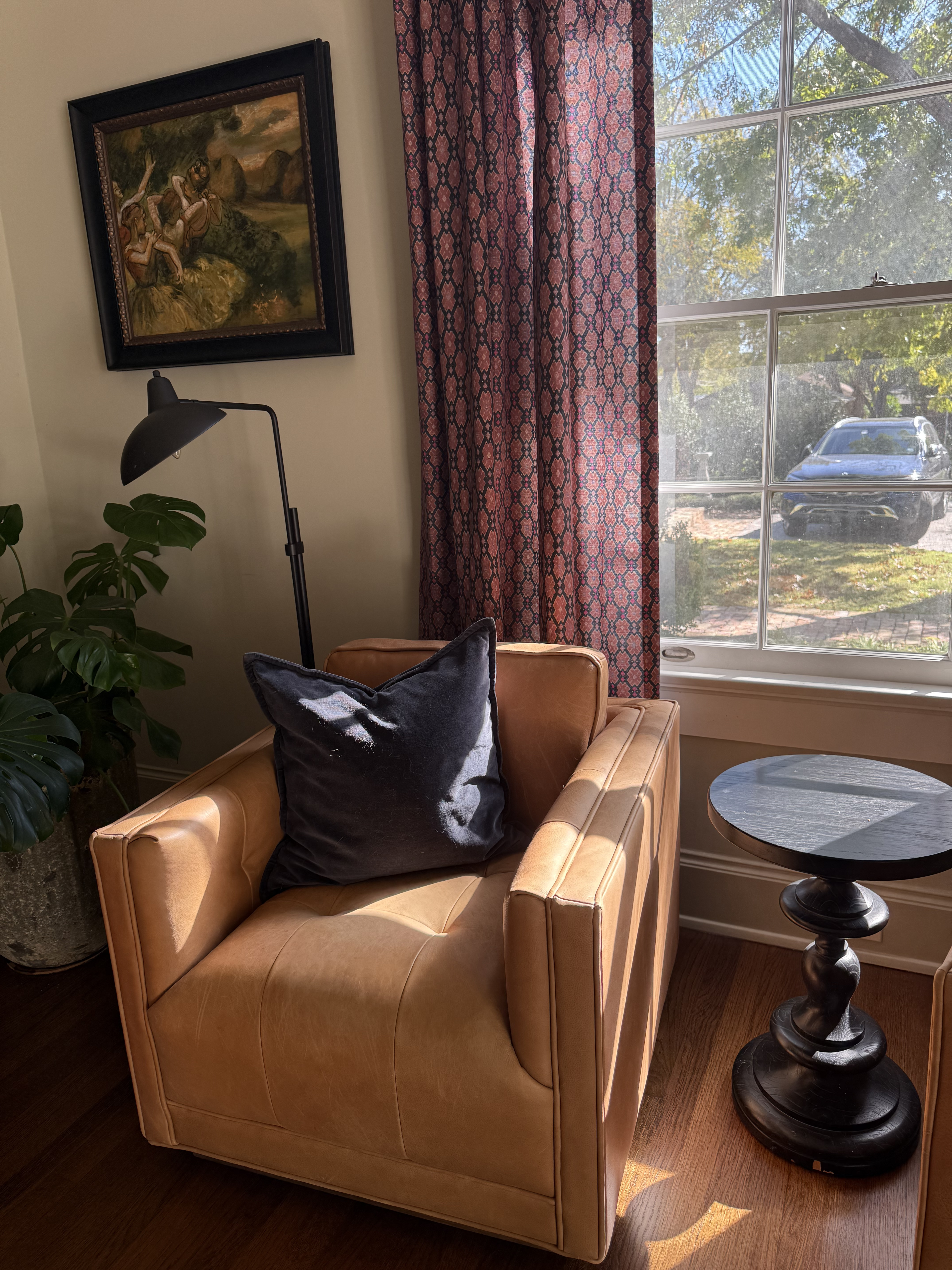 Tan leather swivel chair with velvet pillow, floor lamp, and rose-patterned drapery
