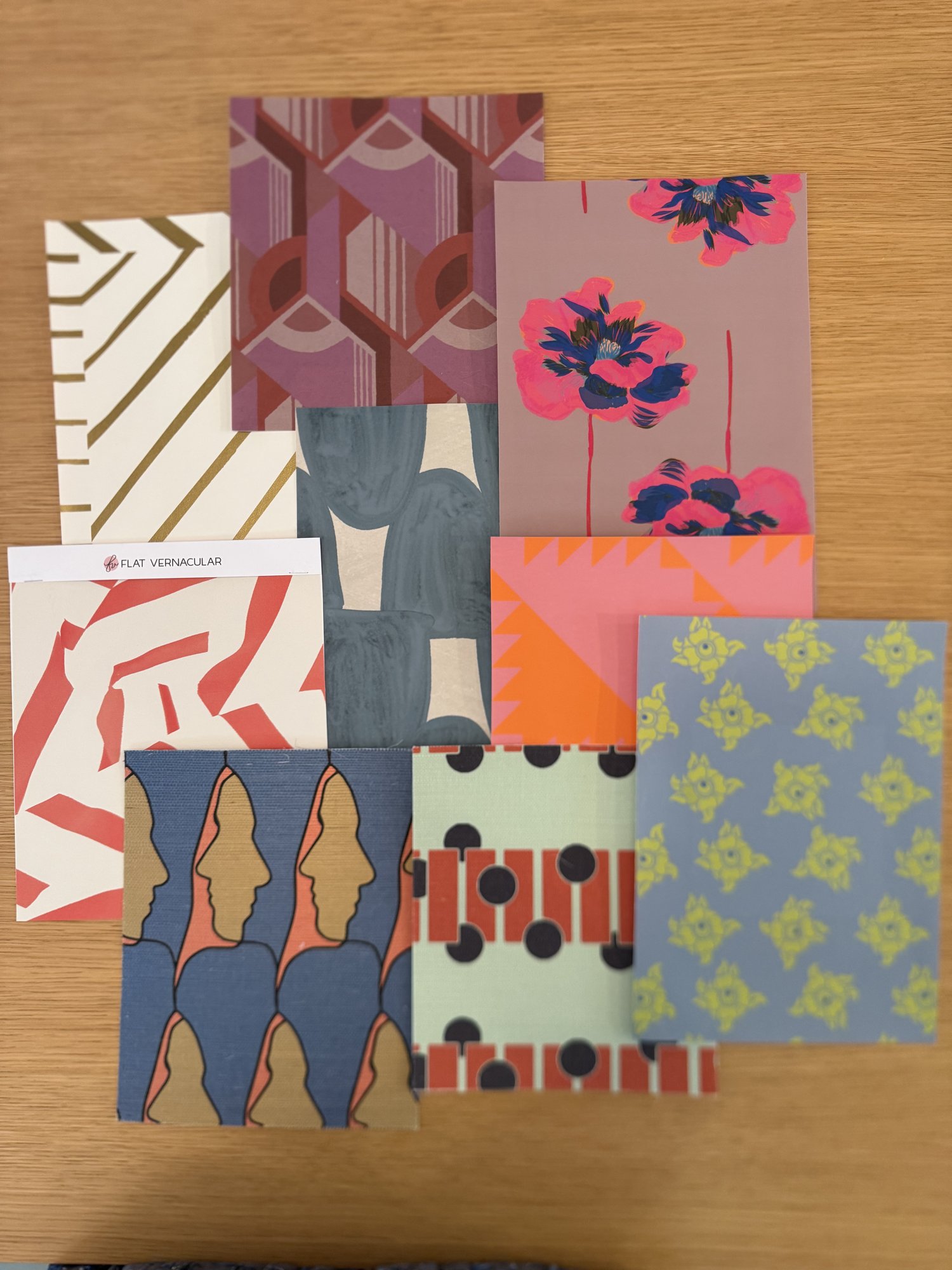 Layered wallpaper samples in pinks, blues, and corals on a light oak table